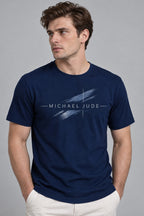 A man wearing a Michael Jude navy blue crewneck t-shirt with a white artistic brushstroke graphic on the chest.